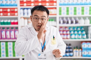 Poster - Chinese young man working at pharmacy drugstore hand on mouth telling secret rumor, whispering malicious talk conversation