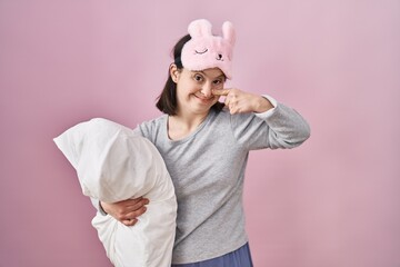 Canvas Print - Woman with down syndrome wearing sleeping mask hugging pillow pointing with hand finger to face and nose, smiling cheerful. beauty concept