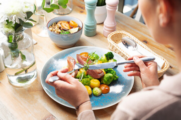 Woman eating lunch, duck meat with vegetables on a plate, at restaurant. Fresh, healthy lunch, selective focus.