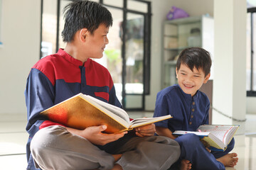 Asian Muslim boy reading Quran and teaching his brother or friend how to read holy Quran inside the mosque