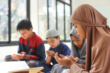 Wall Mural - Asian muslim teen girl praying dua after or before reading Quran together with multiethnic friends during Ramadan feast at mosque