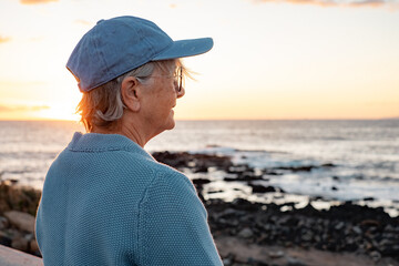 Portrait of relaxed senior woman outdoors at the beach enjoying sunset light looking at the horizon over sea. Happy pensioner woman in serene retirement