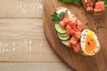 Healthy sandwich with bread or toast, smoked salmon, soft egg, cream cheese, cucumber, radish, black sesame and parsley on old wooden table. Delicious protein fish sandwich for breakfast. Smorrebrod.