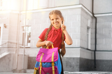 Sticker - Portrait of cute little schoolgirl showing victory gesture outdoors