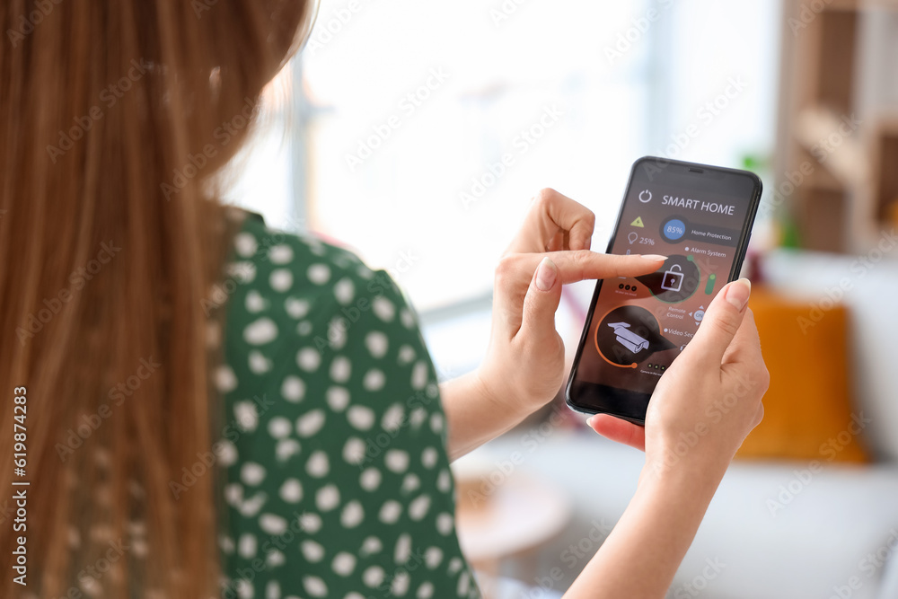 Young woman using mobile phone with smart home security system control panel, closeup