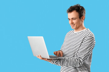 Wall Mural - Young man with laptop on blue  background