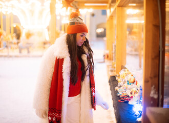 Wall Mural - Charming young woman at the Christmas market next to the New Year tree.