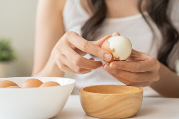 Protein in food, keto diet asian young woman hand peeling, shelling chicken boiled egg, prepares ingredient for breakfast meal on table at home. Removing egg shell, cleaning egg, health care concept.