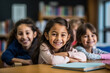© AdriaVidal - Happy latin schoolgirls sitting at the desk in the elementary school classroom, posing, smiling and looking at camera