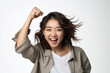 Asian woman with fists raised, showing relief, happiness, and excitement. She is against a white wall, wearing a bright jacket. Joy and enthusiasm can be seen in her eyes.