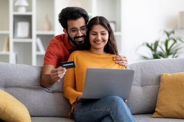 Wall Mural - Indian Couple Making Online Shopping With Laptop And Credit Card At Home