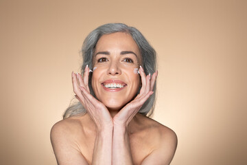 Wall Mural - Face care concept. Cheerful smiling senior woman touching her smooth cheeks, applying moisturizer cream on her face