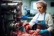Woman working in a butchery, wearing protective clothes and gloves, putting minced meat into a meat grinder
