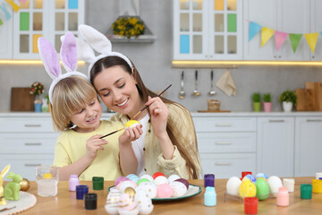 Sticker - Mother and her cute son painting Easter eggs at table in kitchen