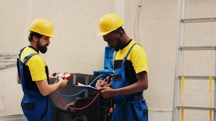 Wall Mural - Adept repairmen working with manifold meters to check air conditioner refrigerant levels, writing result on clipboard. Proficient workers using barometer benchmarking outdoor hvac system tool