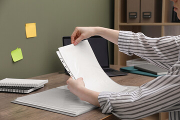 Wall Mural - Woman putting paper sheet into punched pocket at wooden table, closeup