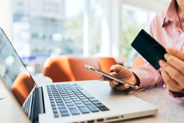 A woman sitting in a café is using her credit card to make online purchases.