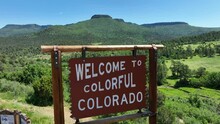 Welcome To Colorful Colorado Sign Along Interstate Highway With Beautiful Scenic Lookout. Aerial Rising Shot Revealing Scenic Mountains In CO.