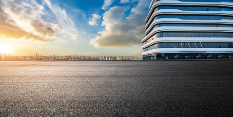 Asphalt road and glass wall with city skyline at sunset