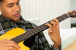 © wavebreak3 - Happy biracial man sitting on bed playing guitar at home