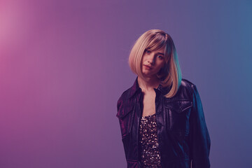 Pretty sexy beautiful blonde woman in leather jacket look at camera posing isolated in blue violet pink color light studio background. Neon party Cyberpunk concept. Copy space