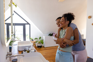 Happy biracial lesbian couple hugging in bathroom