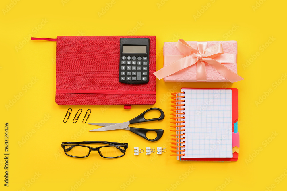Gift box with calculator, eyeglasses and different stationery on yellow background