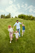 © master1305 - Happy couple, man and woman going for a walk in park with their little children, boy and girl, running, playing on grass. Concept of family, childhood and parenthood, fun, weekends, love, ad