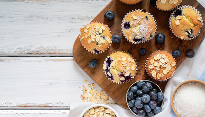 Freshly baked blueberry muffins with almond, oats and icing sugar topping on a rustic white wooden table with berries, brown sugar. Top view