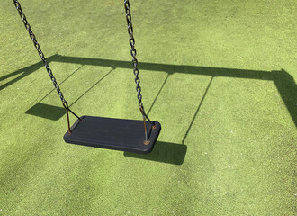 Black swing on green grass at the playground. Green coating on the sports ground. Place to add text