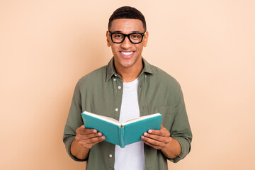 Wall Mural - Photo of positive charming man wear khaki shirt eyeglasses reading interesting book isolated beige color background