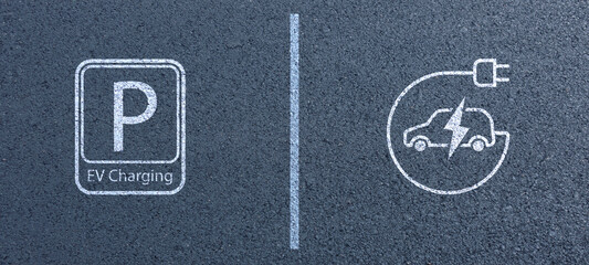 Electric Vehicle Charging Station Sign on Asphalt Background in public area, with parking spaces and road markings denoting charging bays