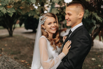 couple in love in the autumn park. Blonde bride in a wedding dress with sleeves. Groom in a classic black suit, white shirt and tie. Smiles and joy