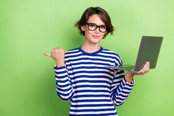 Photo of confident young lady pointing finger empty space hold laptop dell new marketing campaign isolated on green color background
