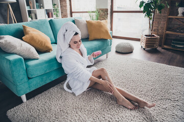 Sticker - Photo of young stunning woman after legs shaving spa salon procedure sitting floor near cozy divan apply cream legs skin indoors