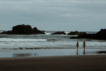 Poster - two girls walking to the wild water on dark beach