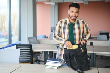 Poster - Young indian student boy reading book studying in college library with bookshelf behind. working on assignment or project