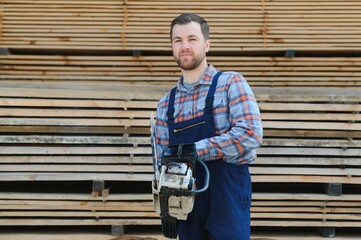 Wall Mural - Carpenter with a saw in his hands stands on a background of cut wooden boards.