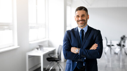 Happy middle aged man manager posing with arms crossed in office and smiling at camera, panorama, copy space