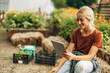 © cherryandbees - Beautiful woman sitting on a hayrick in her garden and using a digital tablet.
