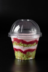 Wall Mural - Takeway cake in a glass with pistachios, strawberry mousse and strawberry confit on black background