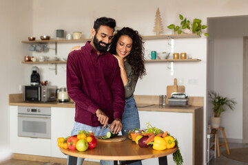 Cooking at home concept. Happy middle eastern woman hugging her husband from behind, arab man preparing healthy meal