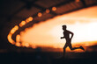 Silhouette of a Male Athlete, an Endurance Runner, Emerges Strong against the Blurred Background of a Modern Sports Stadium