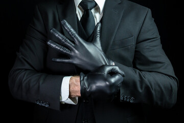 Wall Mural - Portrait of Strong Man in Dark Suit Pulling on Gloves. Mobster Putting on Black Leather Gloves.