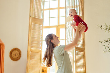 Wall Mural - Beautiful smiling young mother holding, playing with her cute little baby at home, having fun. Love, care, motherhood  concept