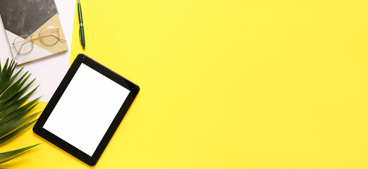 Modern tablet computer, eyeglasses and office stationery on yellow background with space for text