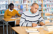 © JackF - Portrait of focused adult latin american student studying in university library, making notes