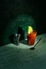 Fototapeta glass of bloody mary with celery on wooden table against dark green background