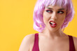 Young woman in wig eating candy on yellow background, closeup