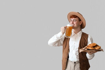 Young man in traditional German clothes with beer and snacks on light background